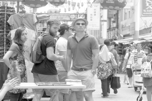Ein belebter Marktplatz mit Menschen und Ständen auf beiden Seiten und Plakaten in der Mitte.