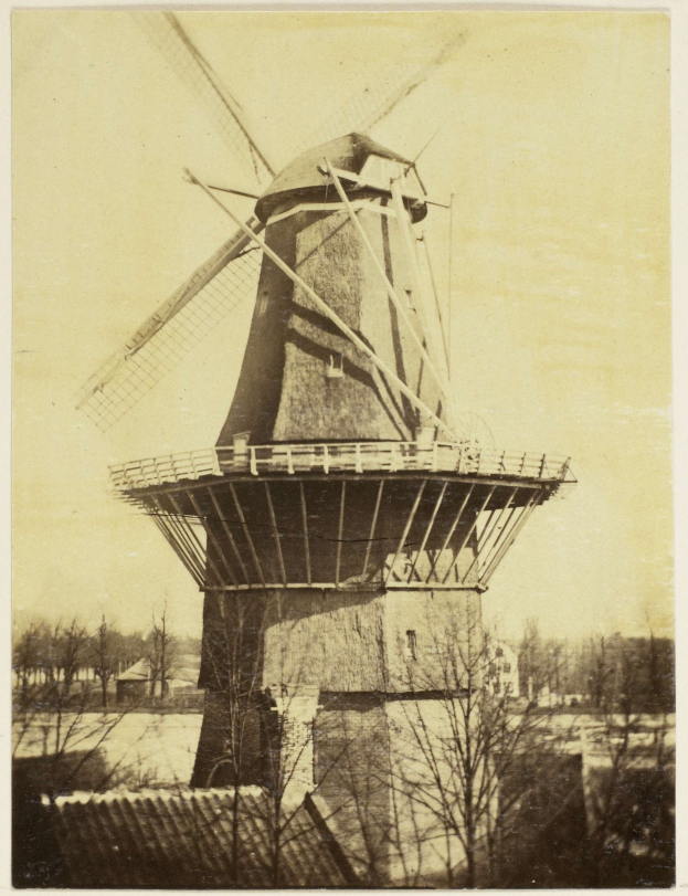 Black and white photo of an old windmill surrounded by trees under a clear sky.