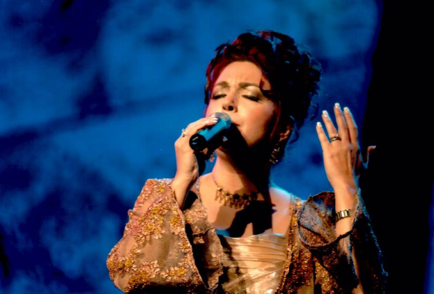 Frau in goldenem Kleid, die auf der ESC-Bühne in ein Mikrofon singt, vor blau-schwarzem Hintergrund.