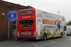Ein weißer und roter Bus steht auf einer Straße mit einer roten Backsteinwand und einem blauen Warnschild im Hintergrund.