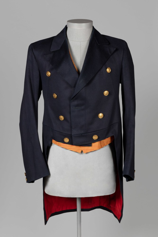 Eine Schaufensterpuppe trägt eine marineblaue doppelreihige Jacke mit goldenen Knöpfen und einem roten Rock, die eine perfekte Passform und hochwertige Stoffe bietet.