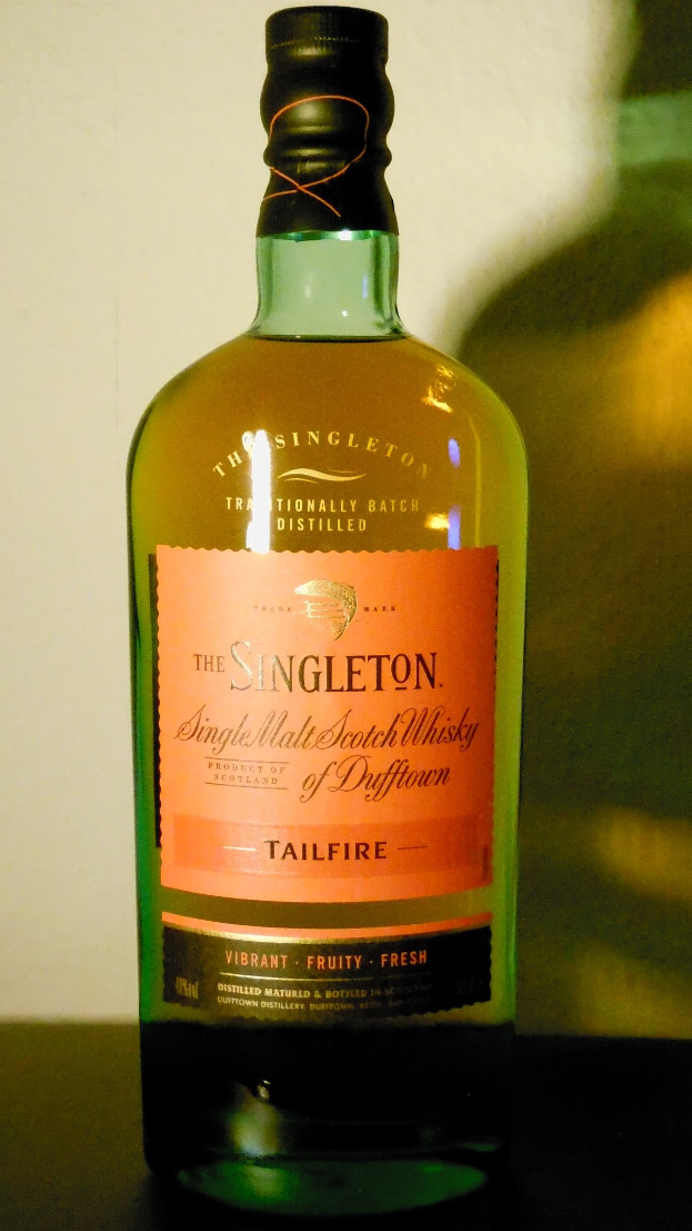 Tiefe Bernsteinflasche Singleton of Dufftown Tailfire Single Malt Scotch Whisky mit schwarzer Beschriftung, die ein Löwen- und Schlosswappen auf einem Tisch zeigt.