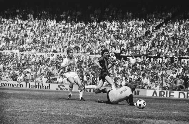 Ein Schwarz-Weiß-Bild einer Gruppe von Männern, die auf einem Feld Fußball spielen, mit Zuschauern im Hintergrund und einer Banner mit der Aufschrift 'Bundesliga 1978-79 Ajax 1-1 Hannover 96'.