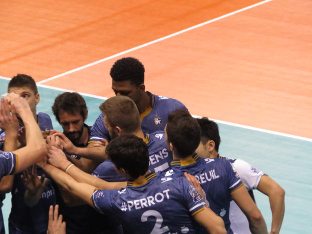 A group of men in blue "Ligue 1" t-shirts celebrating on a volleyball court.