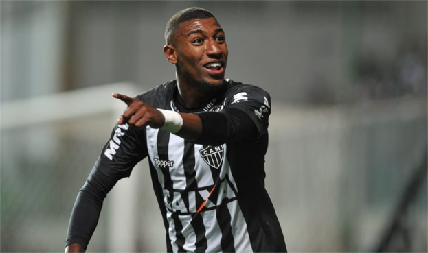 Fußballspieler in schwarzem und weißem gestreiftem Trikot, der grinsend einen Torerfolg feiert, Hintergrund unscharf.