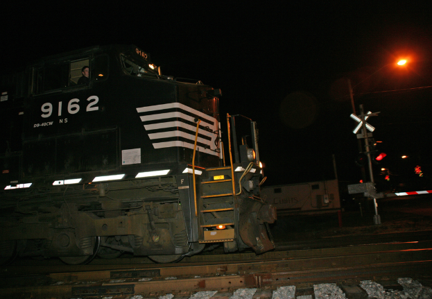Ein Zug auf den Schienen mit einer roten Lampe an einem Pfahl auf der rechten Seite, vor einem dunklen Hintergrund.