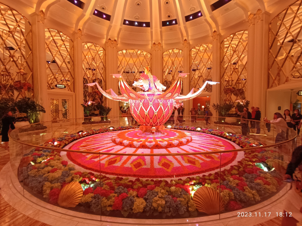 Außenansicht des Bellagio Hotels und Casinos in Las Vegas, Nevada, mit dekorativen Blumenarrangements auf dem Boden, Menschen mit Taschen und beleuchteten Säulen im Hintergrund.