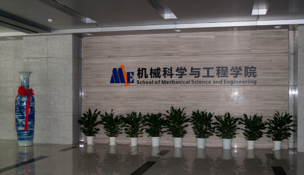 Eine Marmorwand mit einer hölzernen Tafel, auf der ein Logo und der Name eines Ingenieurzweigs zu sehen sind, flankiert von kleinen Pflanzen auf der rechten Seite und einem unbekannten Objekt auf der linken Seite.