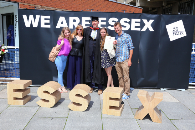 Eine Gruppe von Menschen, die strahlt und ein Zertifikat hält, mit einem Gebäude und einem Netz im Hintergrund.