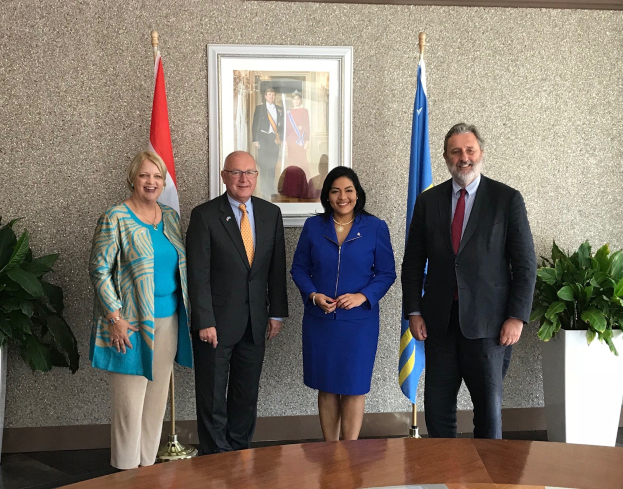 Gruppe von Menschen, die um einen Tisch mit Papieren stehen, umgeben von Fahnen, Topfpflanzen und einem gerahmten Foto an der Wand, was die Unterzeichnung eines U.S.-Kanada-Memorandums von Verständigung anzeigt.