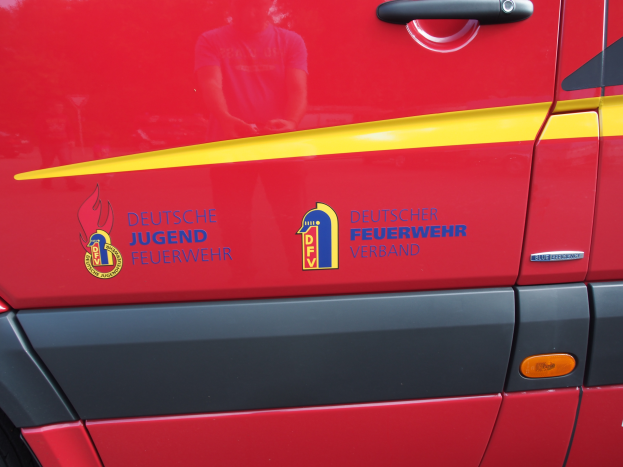 Ein roter Lieferwagen mit einem gelben Streifen, einem Türgriff und einem Logo mit einem Schild mit einem Löwen und einem Lorbeerkranz, mit der Aufschrift "Deutscher Jugendfeuerwehrverband".
