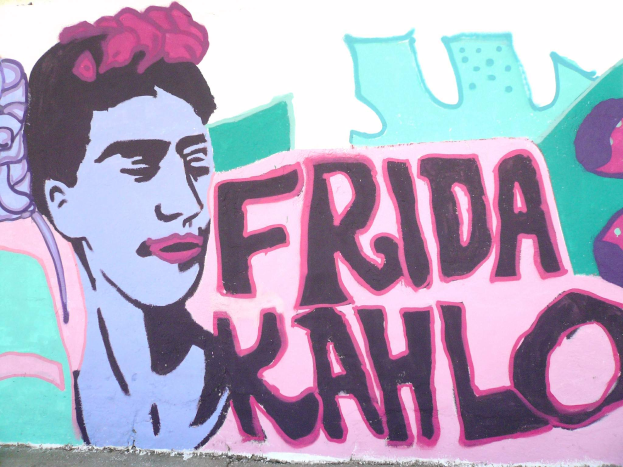 Ein leuchtendes Wandgemälde von Frida Kahlo an einem Gebäude in Mexiko-Stadt, das ihr Porträt mit einer Blume im Haar und den Text 'Fridakahlo' in fetter schwarzer Schrift zeigt.
