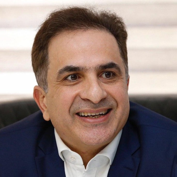 Ein Mann in einem blauen Anzug lächelt in die Kamera und scheint mitten in einem Gespräch zu sein.