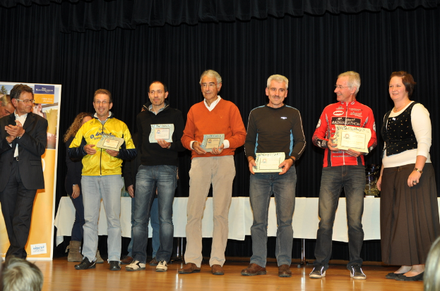 Eine Gruppe von Menschen steht auf einer Bühne und hält Zertifikate, mit einem Banner im Hintergrund, einem Tisch daneben und einem schwarzen Vorhang.