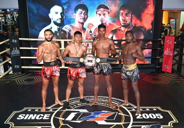 Four men in a boxing ring hold championship belts while a "Muay Thai World Championship" screen displays behind them.