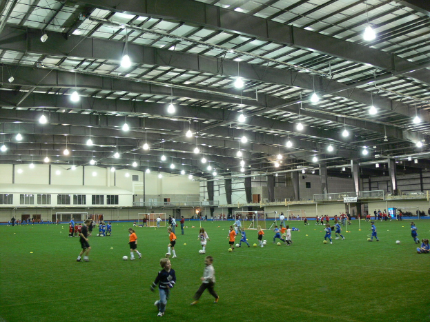 Ein Hallenfußballstadion mit einer Gruppe von Menschen, die mit einem Fußball auf dem Boden spielen, Torpfosten und Beleuchtung auf dem Dach.