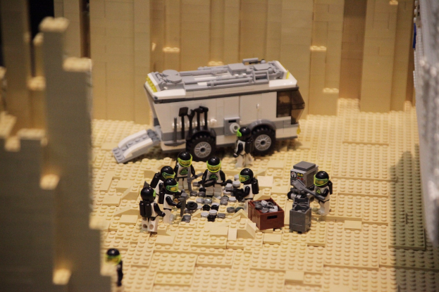 Lego-Modell einer Star-Wars-Szene mit einem Landfahrzeug im Vordergrund und einer Wand im Hintergrund, umgeben von verstreuten Lego-Spielzeugen.