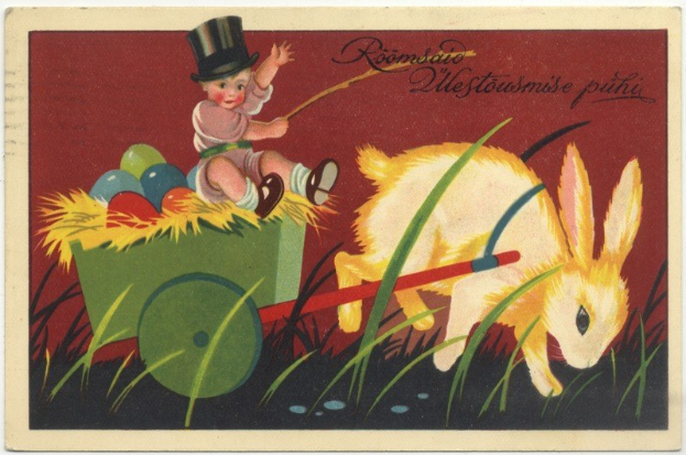 Alte Postkarte mit einem Baby in einem Zylinder, das einen mit bunten Ostereiern gefüllten Handwagen schiebt, begleitet von einem Hasen, mit handgeschriebenen Ostergrüßen.