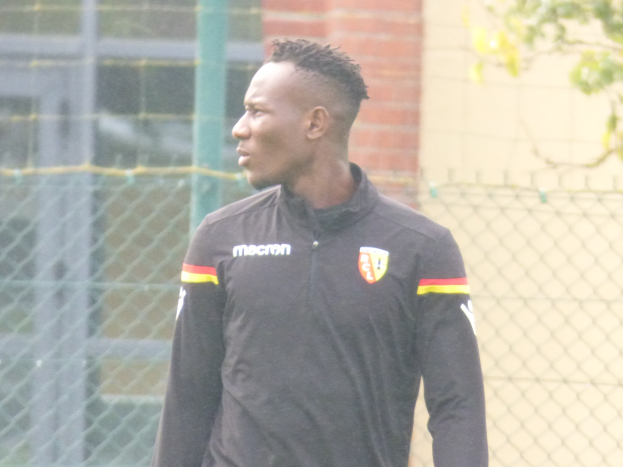 Ein Mann In Einer Schwarzen Jacke Steht Auf Einem Fussballfeld, Umgeben Von Einem Zaun Und Eines Baumes, Und Sieht konzentriert Aus During A Training Session.