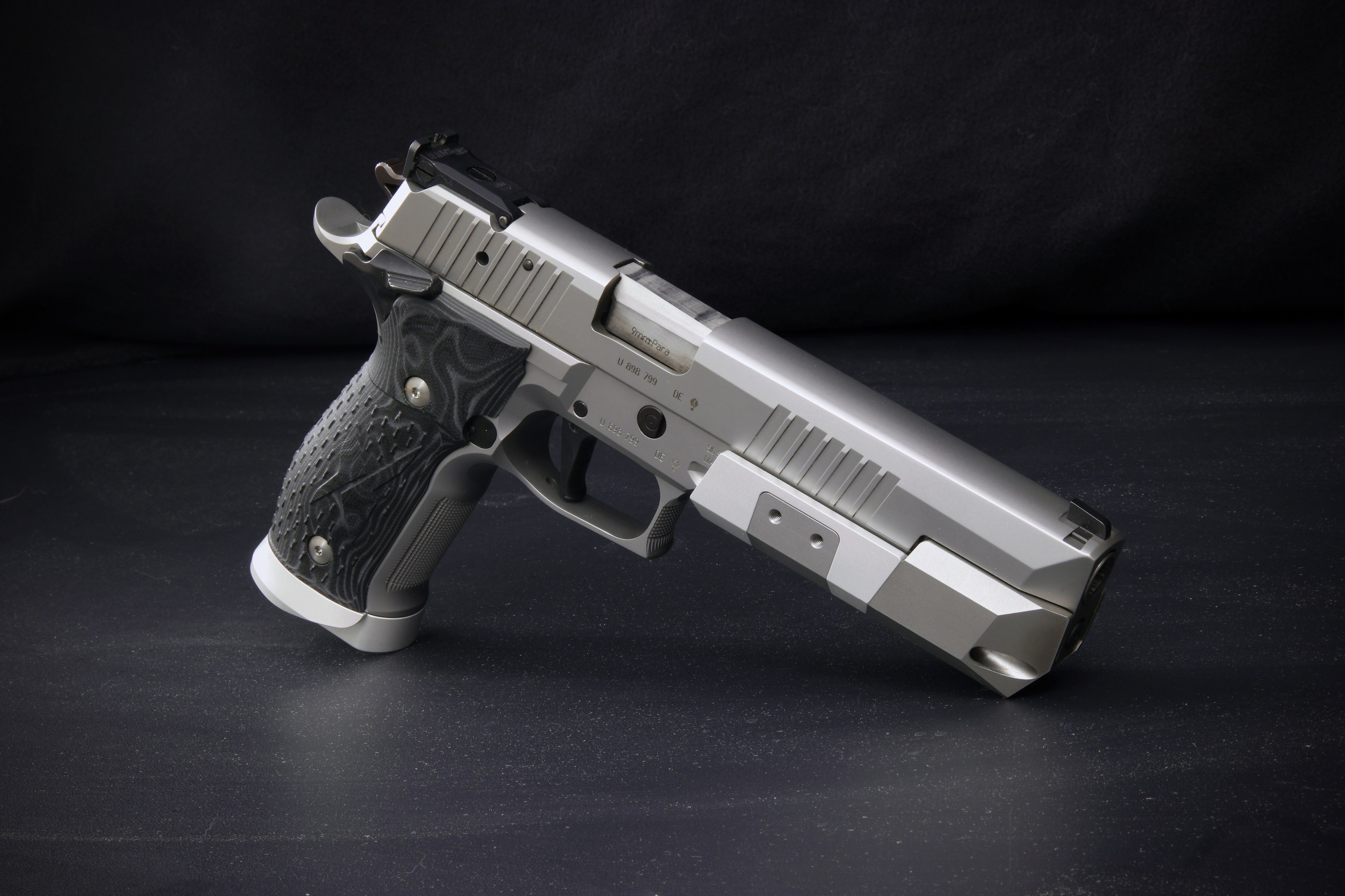 Sig Sauer P226 X-Five 9mm Pistole auf einer schwarzen Oberfläche mit einem schwarzen Hintergrund.