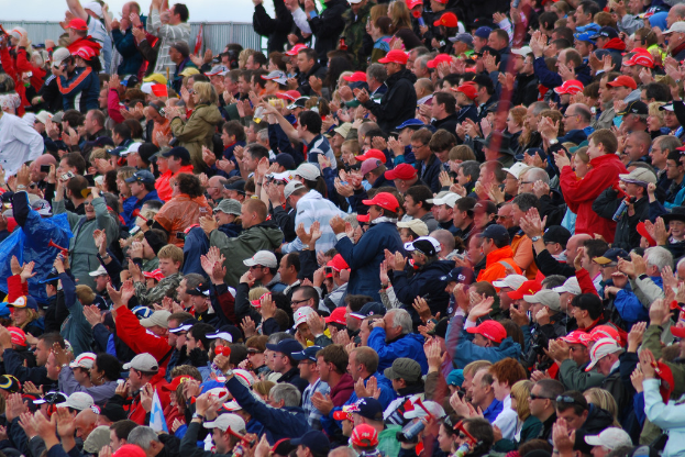 Eine große Menschenmenge, viele mit roten Mützen, versammelte sich vor einem Zaun.