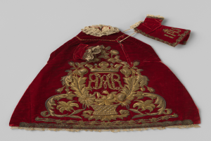 Ein roter Samtmantel mit goldener Stickerei und einer Krone, auf einem weißen Hintergrund, mit detaillierten königlichen Mustern.