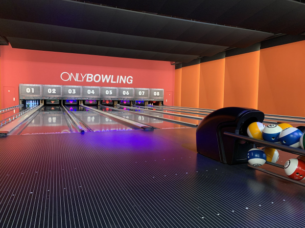 Eine Bowlinganlage mit Bowlingkugeln rechts, Pins in der Mitte und einer textbedeckten Wand im Hintergrund, mit der Decke darüber.