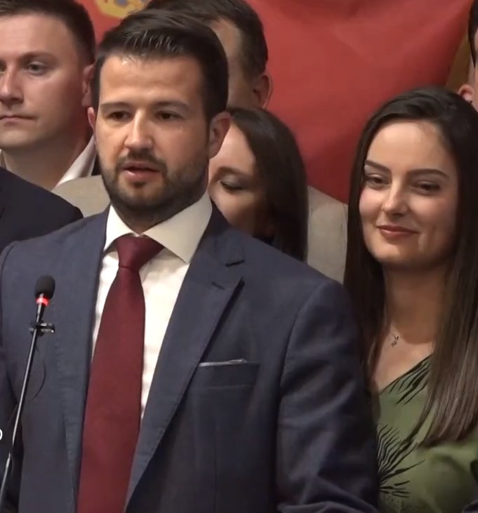 Ein Mann im Anzug spricht an einem Rednerpult mit einem Mikrofon zu einer Menge hinter einem Banner, wahrscheinlich über ein Regierungsozialmediaverbot.