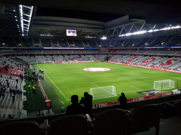 Großes Stadion voller Zuschauer bei einem Fußballspiel im Estadio Santiago Bernabeu in Madrid, Spanien, mit sitzenden und stehenden Zuschauern unter Stadionbeleuchtung und einem großen Überkopfbildschirm.