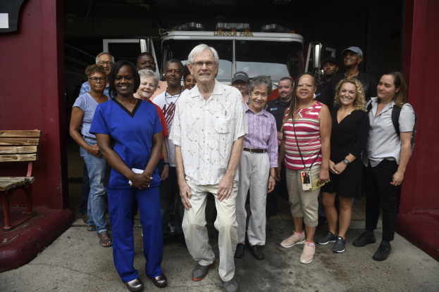 Gruppe von Freiwilligen vor einem Feuerwehrauto mit einer Bank links und einer Wand im Hintergrund.