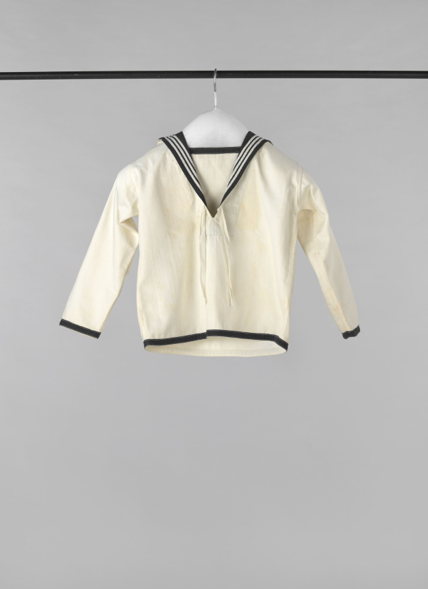 Weißes Seemanns-Jackett mit Kragen, langen Ärmeln und Knopfleiste, das an einer Wäscheleine an einem weißen Hintergrund hängt, aus leichtem Rippenstoff hergestellt.