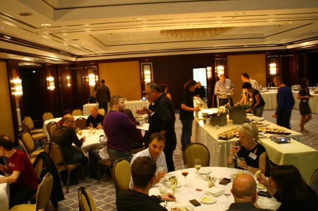 Ein Restaurant mit Tischen und Stühlen, an denen Gruppen von Menschen sitzen und essen, und einige stehen um einen zentralen Tisch mit verschiedenen Speisen herum.