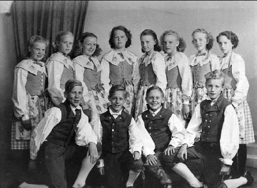 Schwarz-weißes Foto von Kindern, die vor einer Vorhangwand posieren, mit dem Text "1930er Kinder-Schule" unten.