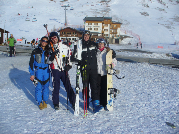 Vier Personen posieren für ein Foto mit Schlittschuhen und Werkzeugen vor einer schneebedeckten Bergkulisse.