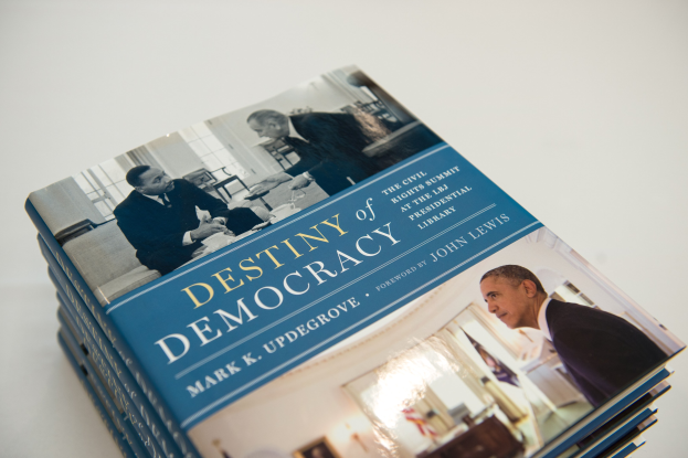 Ein Stapel Bücher mit dem Titel "Zukunft der Demokratie" mit Text und Bildern von Menschen auf den Umschlägen, auf einer weißen Oberfläche plaziert.