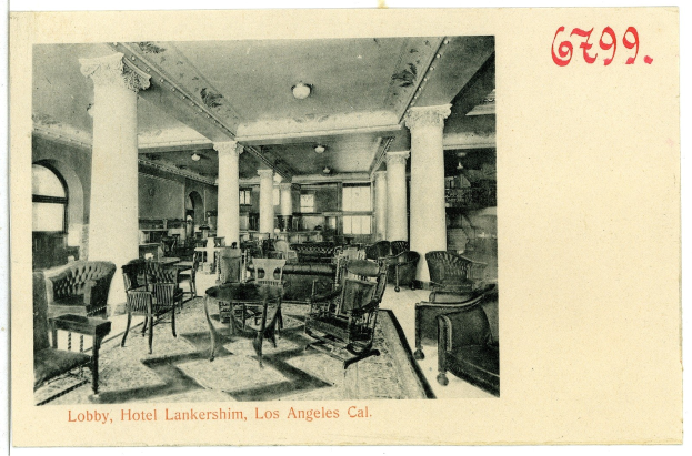 Black and white photo of a hotel lobby in Los Angeles with chairs, tables, pillars, ceiling lights, and windows on the left.
