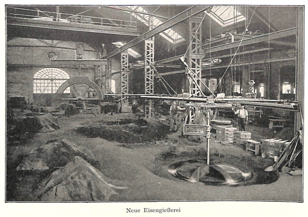 Schwarzes und weißes Foto einer Fabrikhalle mit Arbeitern, die Maschinen bedienen, umgeben von Metallstangen und -rohren, beschriftet mit "Neue Eisenglebeerei, die erste Fabrik in Deutschland" unten.
