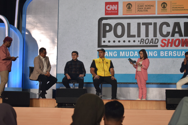 Eine Gruppe von Menschen sitzt auf einer Bühne, einige stehen an einem Podium, und im Hintergrund ist ein Schild mit der Aufschrift "Cnn Political Road Show."