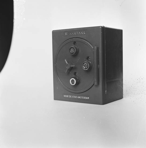 Ein Schwarz-Weiß-Foto einer rechteckigen Sicherheitsschachtel auf einer weißen Oberfläche, mit einem Griff oben, einem Schloss an der Vorderseite und einem Schlüsselloch in der Mitte.