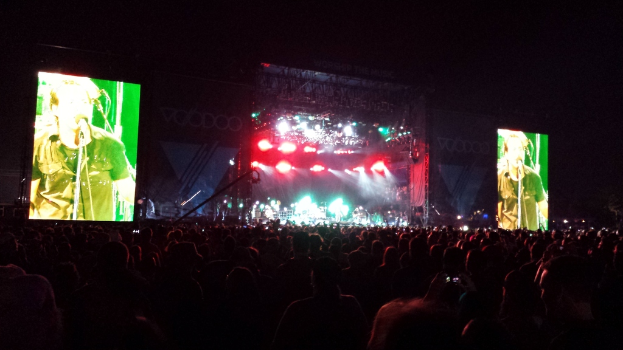 Ein Konzertbild mit einer Menge unten, einem großen Bildschirm links und einem weiteren Bildschirm rechts.