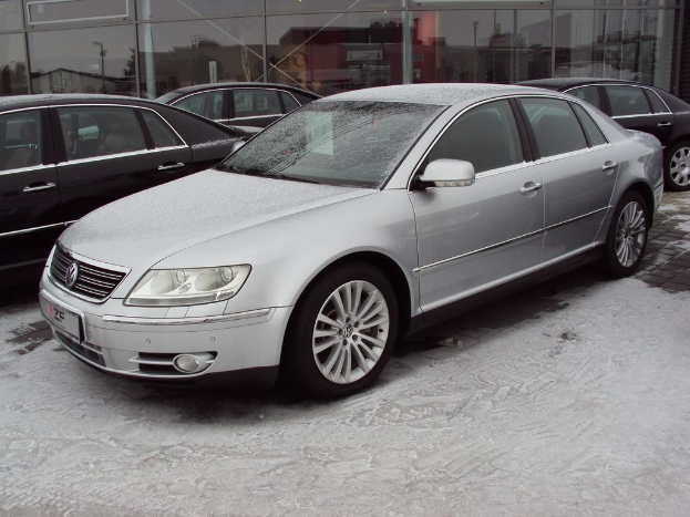 Ein Auto steht auf einem verschneiten Gehweg vor einem Glasgebäude mit drei anderen Autos im Hintergrund.