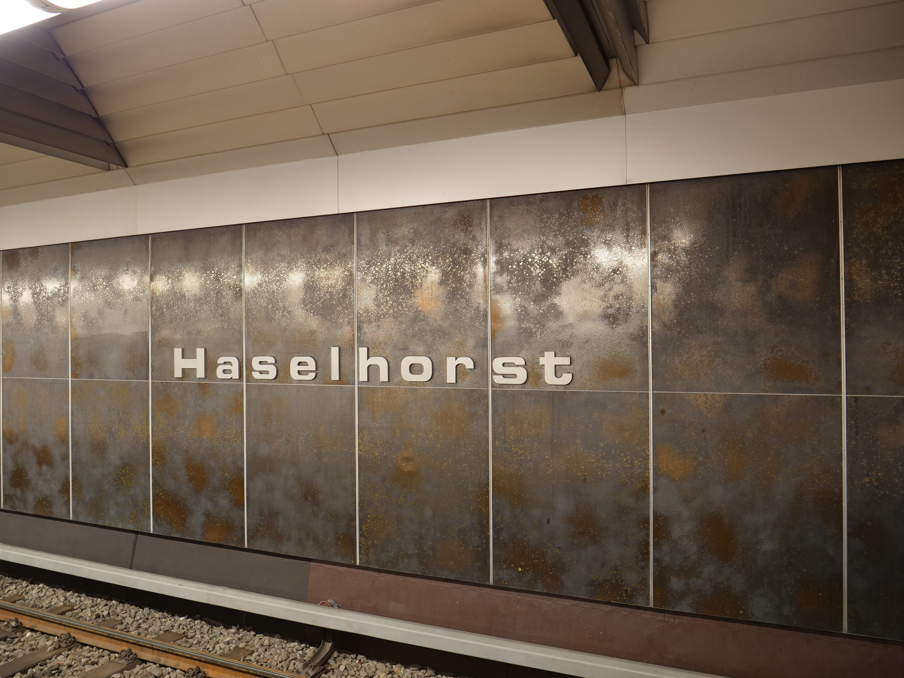 A train station platform with a "Haselhorst" sign illuminated by overhead lights, located in Berlin, Germany.