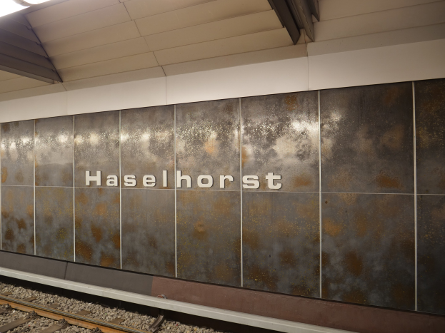 A train station platform with a "Haselhorst" sign illuminated by overhead lights, located in Berlin, Germany.