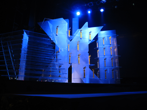 Eine Bühne für eine Preisverleihung mit dunklem Hintergrund, beleuchtet von ein paar Lichtern und verschiedenen, zur Veranstaltung gehörenden Gegenständen.