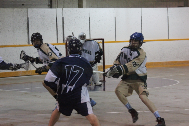 Personen mit Helmen und Stöcken scheinen in einem Innenraum mit einem Netz im Hintergrund zu kämpfen.