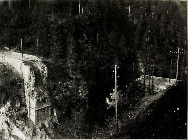 Ein Schwarz-Weiß-Foto einer Brücke über einen Fluss mit Bäumen, Pfählen und Felsen im Hintergrund und einem Text am unteren Rand, der "1930er-Jahre-Brückenbau" lautet.