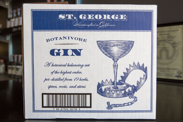 Ein Plakat mit Text steht vor Regalen, die mit vielen Flaschen gefüllt sind.