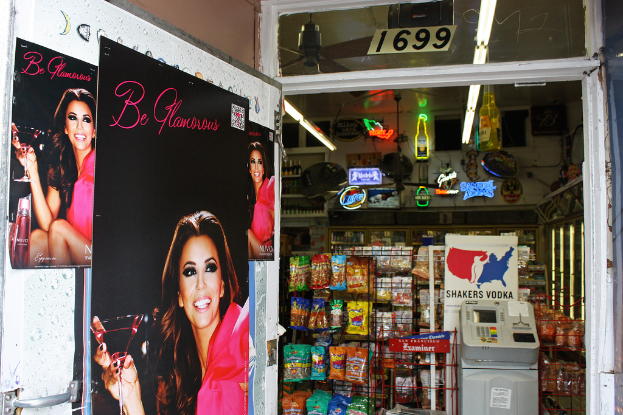 Eine Innenaufnahme mit einer Tür, die Plakate einer Frau auf der linken Seite, verschiedene Ladengüter in der Mitte, einem Geldautomaten und einem Textschild auf der rechten Seite und einer Nummernleiste oben.