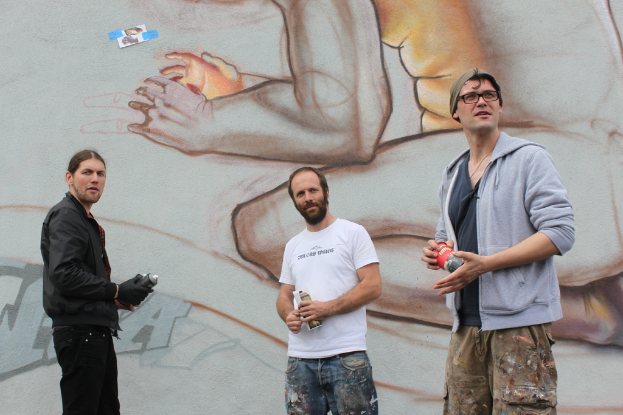 Menschen mit Farbsprühflaschen vor einer mit Graffiti bedeckten Wand.