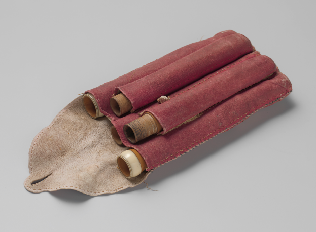 Ein roter Lederbeutel mit Griff, der drei Toilettenpapierrollen enthält, vor einem weißen Hintergrund.